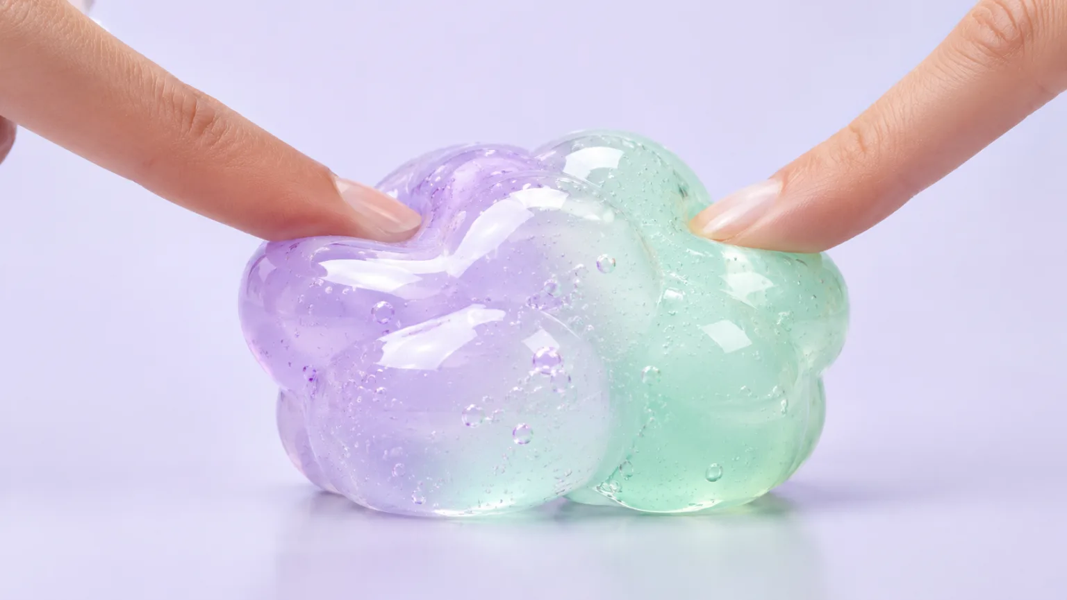 Glossy lavender and mint squishy toy pressed by fingertips in a soft studio